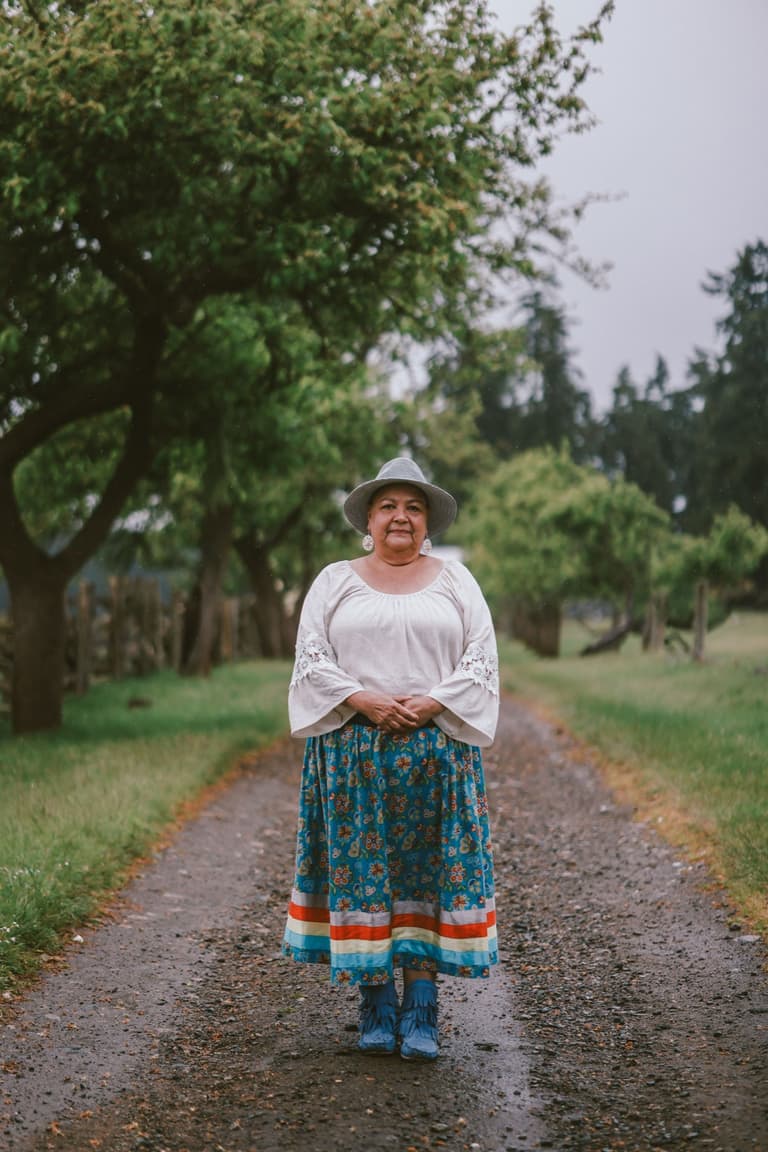 A woman in a hat and a ribbon skirt on an orchard lane