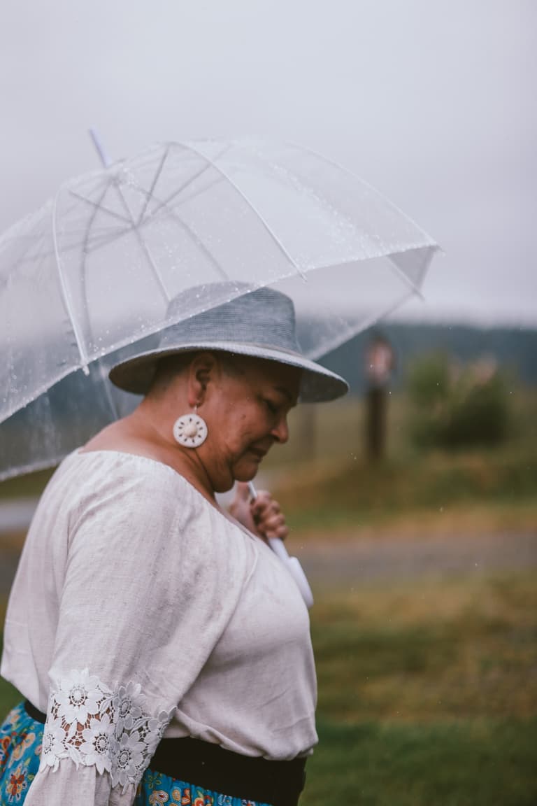 A woman in a wide brimmed hat, in profile under a clear umbrella