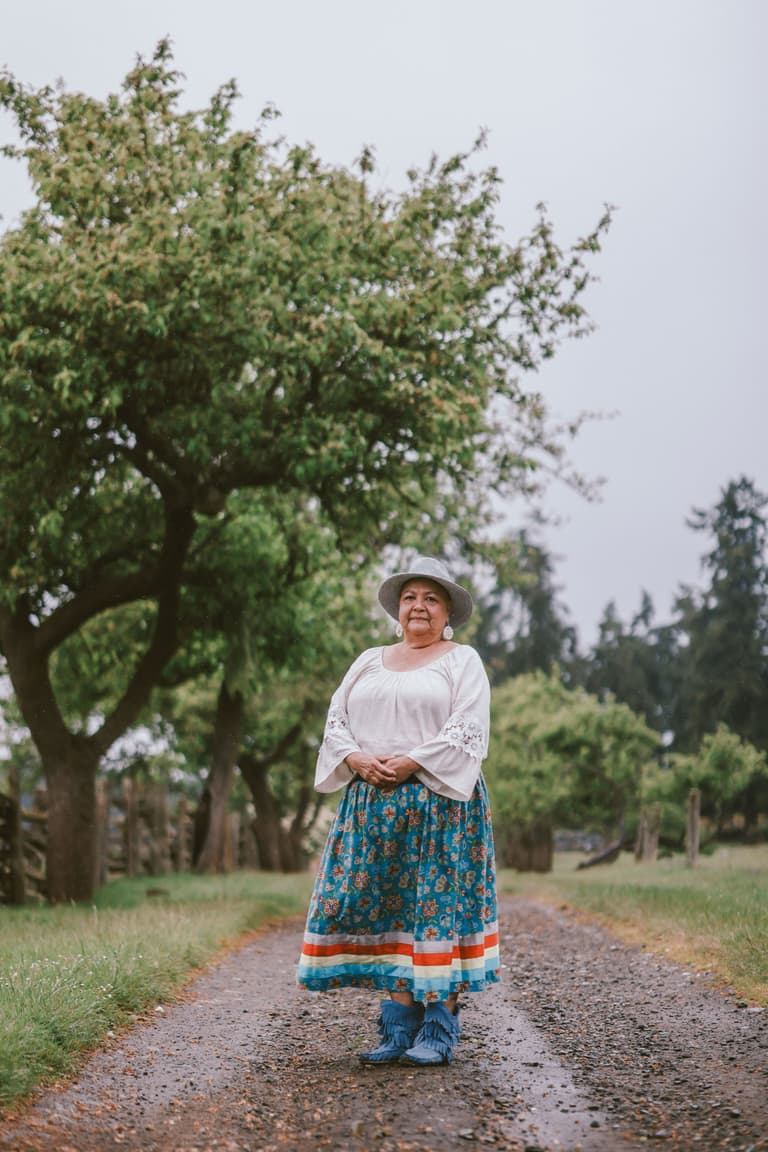 Marilyn in a ribbon skirt, standing on an orchard lane