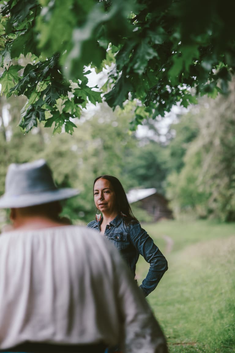 Two women standing together on the grass beside an old barn