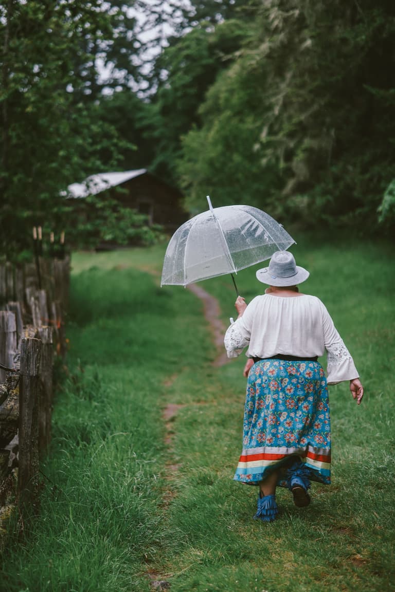 Two women in ribbon skirts standing together on a grass path
