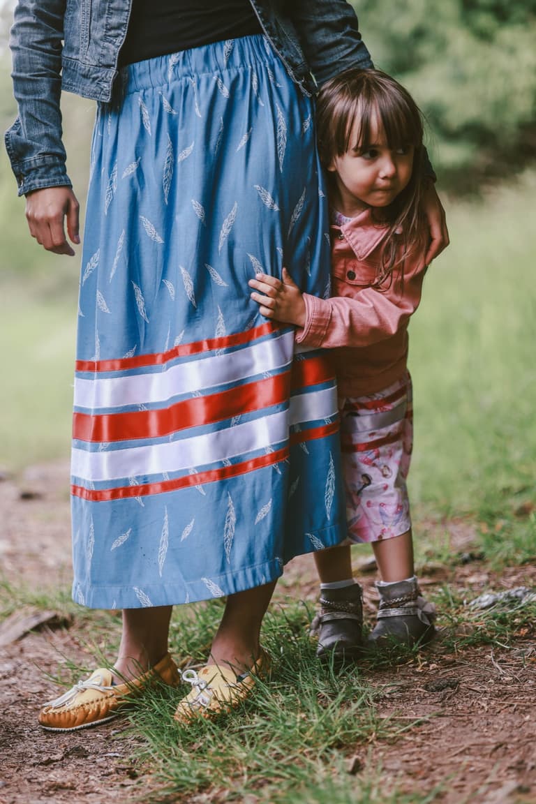 Detail of a blue ribbon skirt with red and white satin bands, a child holding the hem